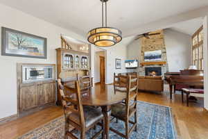 Dining space featuring ceiling fan, vaulted ceiling, light wood-type flooring, and a stone fireplace