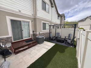View of patio with central air condition unit and fence with turf