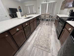 Kitchen featuring electric range oven, a sink, light stone counters, black dishwasher, and light wood-style flooring