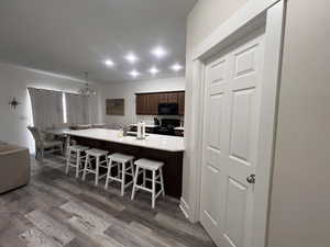 Kitchen featuring dark wood-style flooring, a kitchen bar, dark brown cabinets, black appliances, and an inviting chandelier