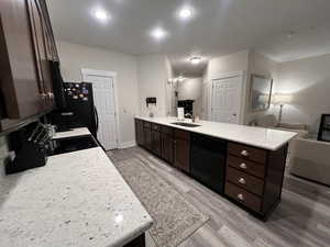 Kitchen with dark brown cabinetry, a sink, a peninsula, wood finished floors, and black appliances