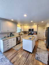 Kitchen featuring a sink, a textured ceiling, a center island, stainless steel appliances, and light wood-type flooring