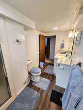 Bathroom with vanity, toilet, a textured ceiling, a shower stall, and wood finished floors