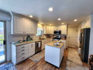 Kitchen featuring a sink, a center island, stainless steel appliances, decorative backsplash, and hardwood / wood-style flooring