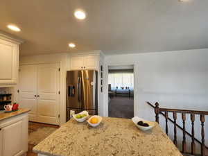 Kitchen with light stone countertops, wood finished floors, stainless steel fridge with ice dispenser, white cabinets, and recessed lighting