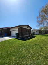 View of side of property with a lawn, an attached garage, concrete driveway, and brick siding