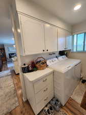 Washroom with cabinet space, a brick fireplace, washing machine and dryer, and hardwood / wood-style flooring