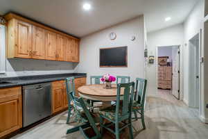 Kitchen with stainless steel dishwasher, light wood finished floors, vaulted ceiling, and dark countertops