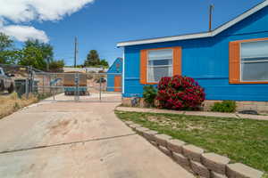 View of property exterior featuring concrete driveway, a lawn, fence, and a gate