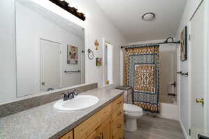 Full bathroom with vanity, shower / bath combo with shower curtain, toilet, and wood finished floors