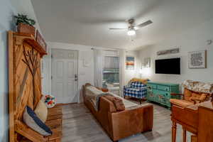 Living area featuring a ceiling fan, a textured ceiling, wood finished floors, and lofted ceiling