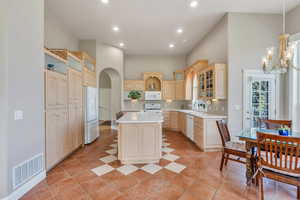 Kitchen with white appliances, light countertops, visible vents, and a towering ceiling