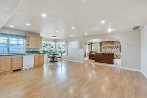 Kitchen with visible vents, light wood-style floors, white dishwasher, arched walkways, and a sink