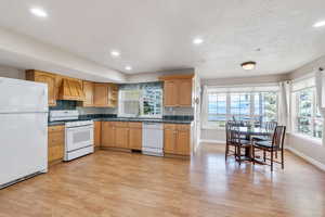Kitchen with dark countertops, white appliances, light wood-style flooring, baseboards, and custom range hood