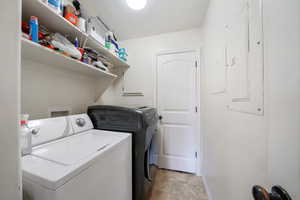 Laundry area with laundry area, baseboards, electric panel, and washer and dryer
