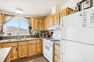 Kitchen with a sink, light countertops, under cabinet range hood, white appliances, and light wood-style flooring