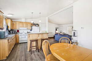 Kitchen with lofted ceiling, a kitchen island, white appliances, dark wood-type flooring, and under cabinet range hood