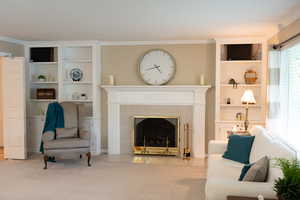 Carpeted living area featuring built in features, ornamental molding, and a fireplace