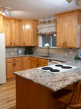 Kitchen with a sink, light stone counters, freestanding refrigerator, and light wood-type flooring