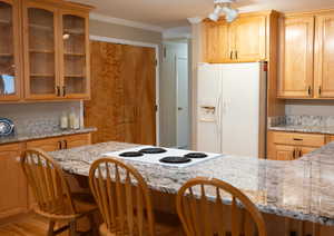 Kitchen featuring white appliances, light stone countertops, ornamental molding, and glass insert cabinets