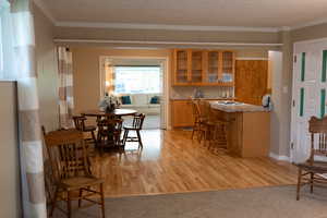 Kitchen featuring ornamental molding, glass insert cabinets, a breakfast bar area, brown cabinets, and light wood-style flooring