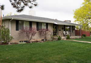 Single story home featuring a porch, a chimney, fence, a front lawn, and a shingled roof
