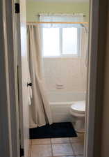 Bathroom with tile patterned floors, toilet, and shower / tub combo with curtain
