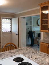 Kitchen with crown molding, carpet, light stone counters, and glass insert cabinets
