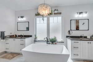 Full bathroom featuring a freestanding bath, a sink, tile patterned floors, a chandelier, and two vanities