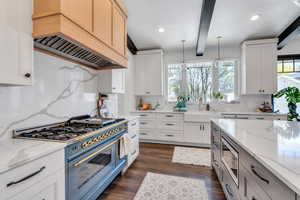 Kitchen featuring appliances with stainless steel finishes, a sink, premium range hood, decorative backsplash, and beamed ceiling