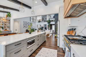 Kitchen with beam ceiling, stainless steel microwave, open floor plan, range hood, and dark wood-type flooring