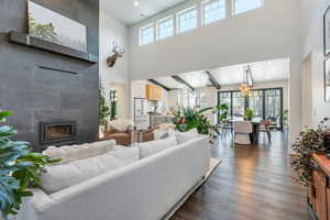 Living area featuring dark wood-style flooring, a fireplace, a high ceiling, recessed lighting, and a notable chandelier