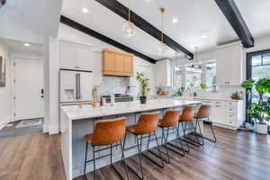 Kitchen with white cabinets, a breakfast bar, dark wood finished floors, decorative light fixtures, and vaulted ceiling with beams