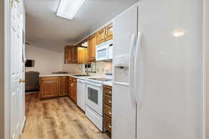 Kitchen with a textured ceiling, light wood-type flooring, a sink, lofted ceiling, and white appliances