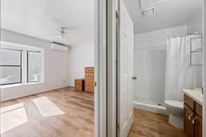 Full bath featuring wood finished floors, toilet, ceiling fan, tiled shower, and a wall mounted AC