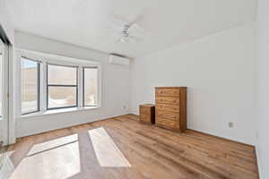 Unfurnished bedroom with wood finished floors, baseboards, ceiling fan, and a wall unit AC