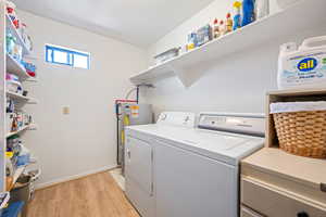 Laundry room with laundry area, light wood finished floors, water heater, and washing machine and dryer