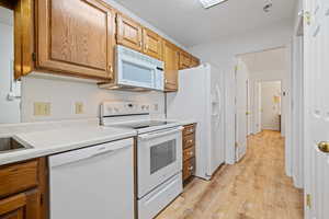 Kitchen featuring light countertops, light wood-type flooring, white appliances, and brown cabinetry