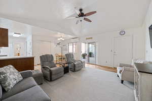 Living room featuring vaulted ceiling, light carpet, ceiling fan with notable chandelier, and a wall mounted air conditioner