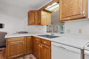 Kitchen with white dishwasher, light countertops, a sink, light wood-style flooring, and vaulted ceiling