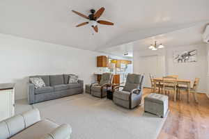 Living area featuring a wall unit AC, ceiling fan with notable chandelier, light wood-type flooring, and lofted ceiling