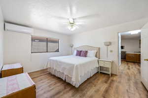 Bedroom featuring a textured ceiling, a wall unit AC, baseboards, and light wood finished floors