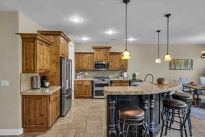 Kitchen featuring brown cabinets, stainless steel appliances, a textured ceiling, and tasteful backsplash