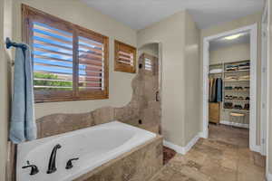 Bathroom featuring a walk in closet, a shower stall, baseboards, a whirlpool tub, and stone tile flooring