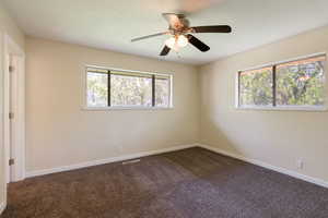 Primary bedroom featuring dark colored carpet, baseboards & ceiling fan