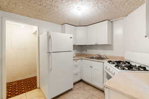 Kitchen featuring a sink, white cabinetry, white appliances, and light countertops