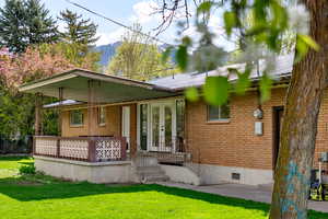 Rear view of house featuring brick, french doors, Stairs to basement, a mountain view, and a lawn