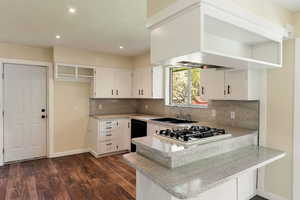 Kitchen featuring dark wood-style flooring, dishwasher, a sink, a peninsula, and stainless steel gas stovetop