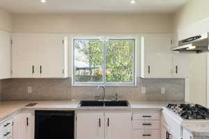 Kitchen with dishwasher, a sink, light countertops, under cabinet range hood, and white cabinetry