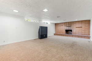 Unfurnished family room featuring baseboards, light carpet, and a brick fireplace